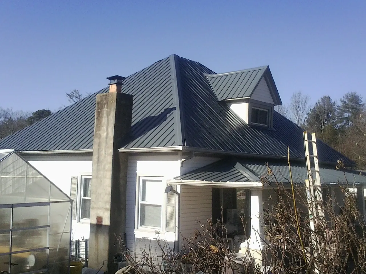 Dark blue standing seam metal roof on a white farmhouse with dormer — Slate & Tile Roof Repair by Roofing Brothers in Fruitland