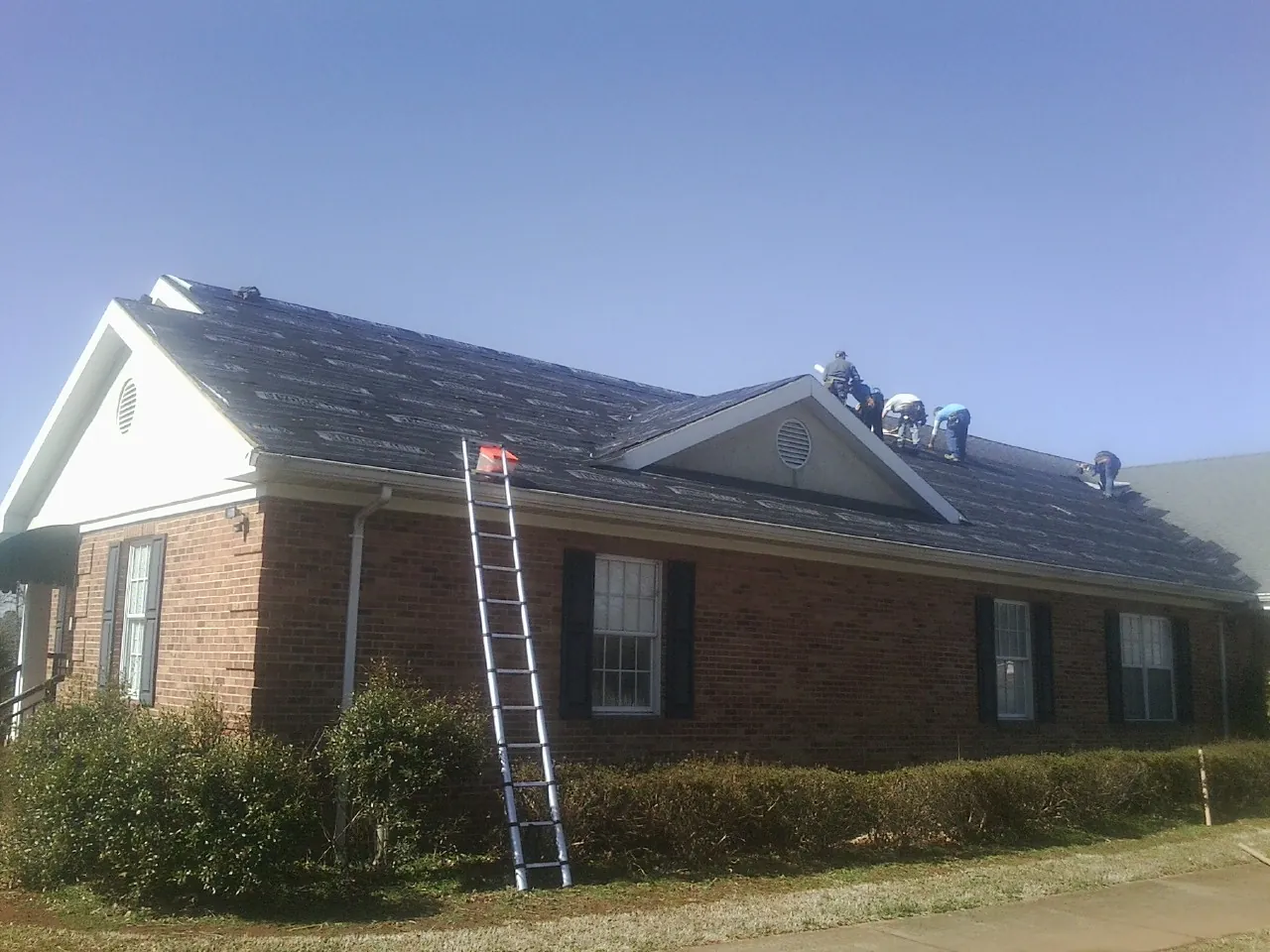 Crew tearing shingles off a brick ranch roof with a ladder set — Emergency Roof Repair work by our crew in Fruitland