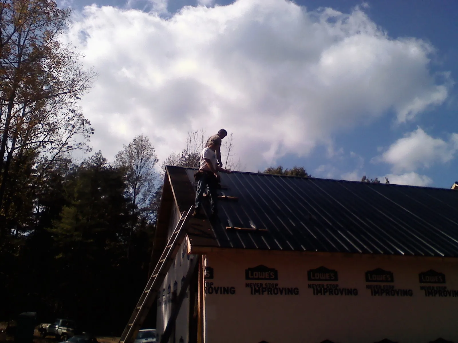 Roofer fastening dark metal panels high against a cloudy sky, from a Roof Inspection job in Fruitland