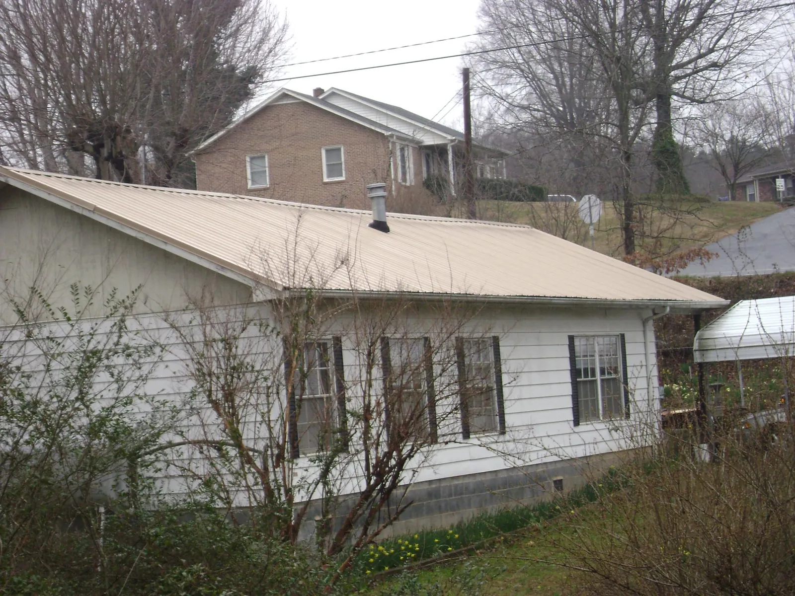 Tan metal roof on a white sided house set into a hillside — Commercial Roofing by Roofing Brothers in Fruitland